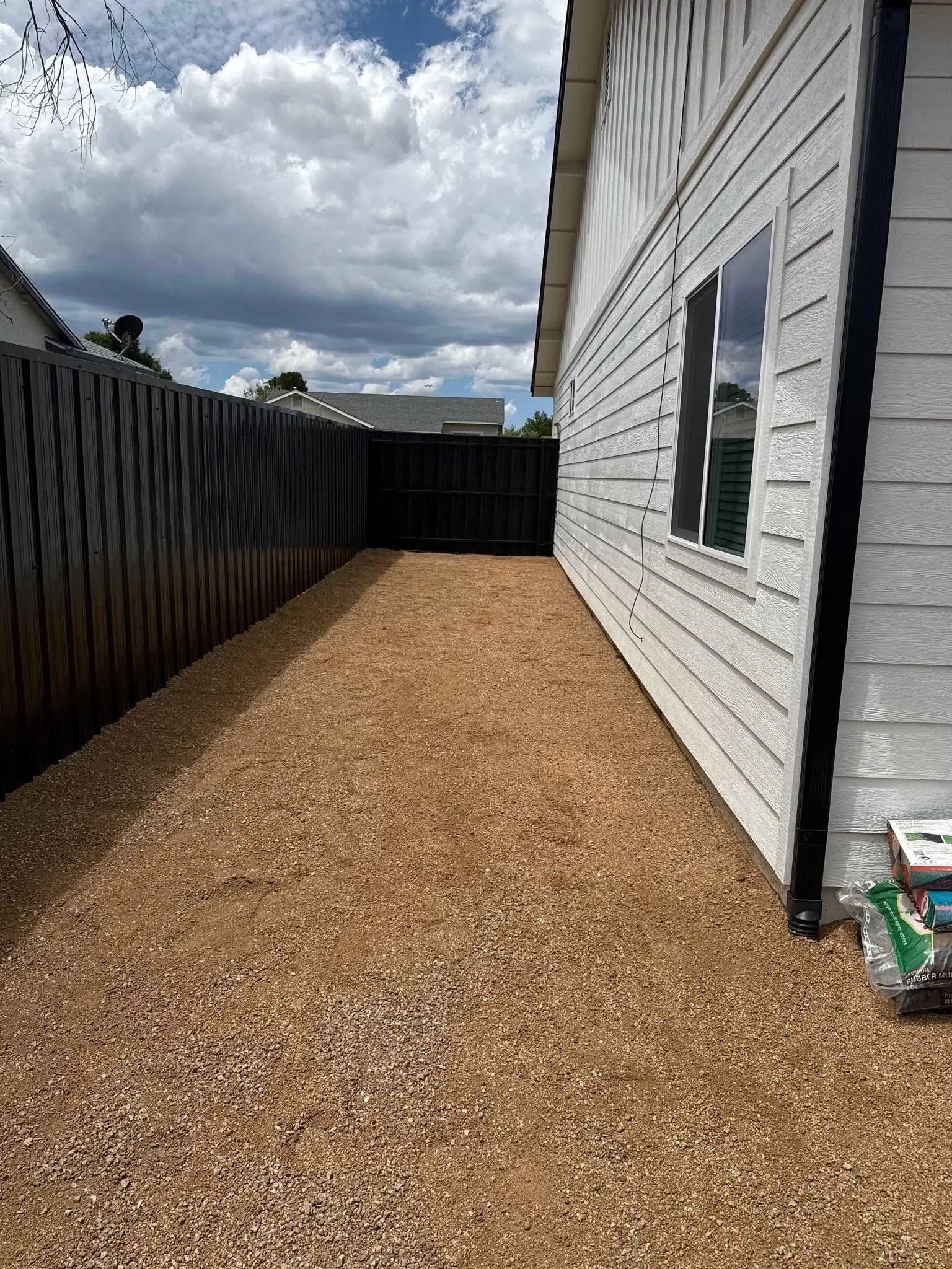 Tan gravel patio with black metal fence and white house siding