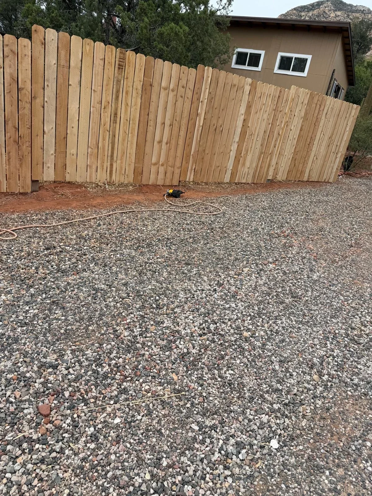 New cedar privacy fence with vertical boards and gravel base preparation at residential property