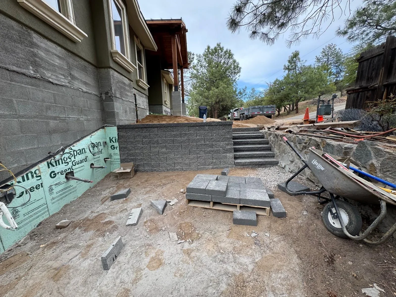 Gray concrete block retaining wall under construction with stepped stone pathway and gravel base