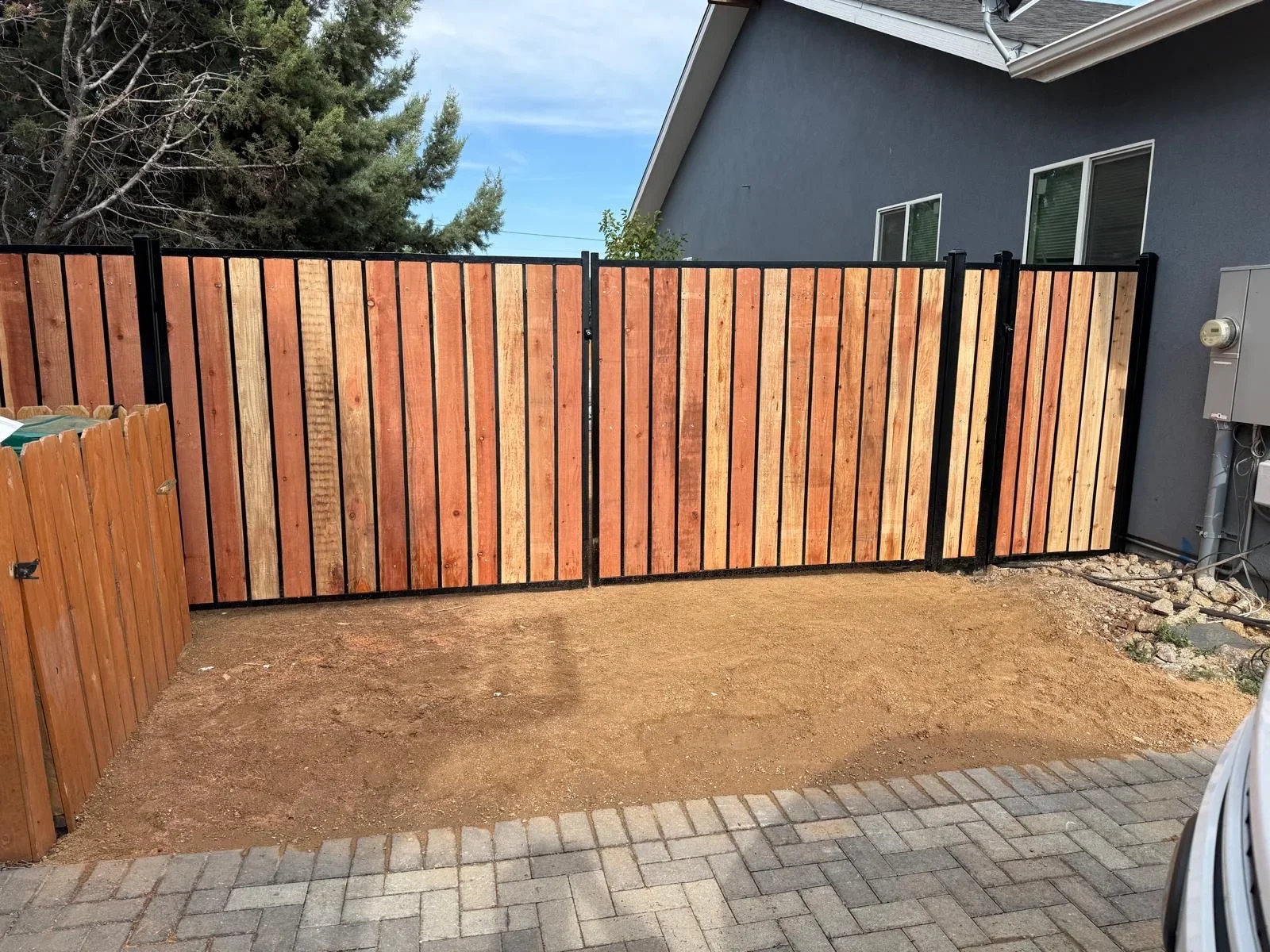 Cedar wood vertical slat driveway gate with black metal frame installed at residential property