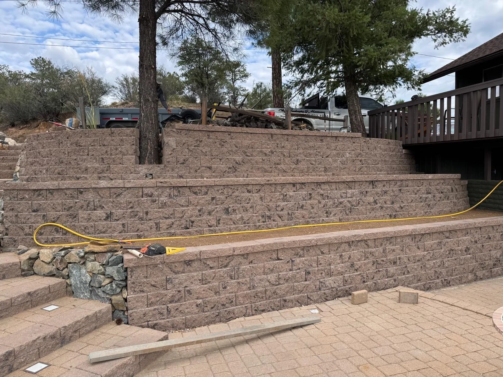Tan concrete block retaining wall with yellow drainage line and paver patio base